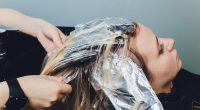 Closeup of hairdresser hands separating strands of hair of beautiful young woman with aluminium foil before change the hair color.