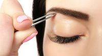 Young woman plucking eyebrows with tweezers close up