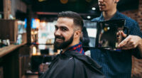 Good looking young adult man getting a hair and beard styling and dressing treatment by professional hairstylist.